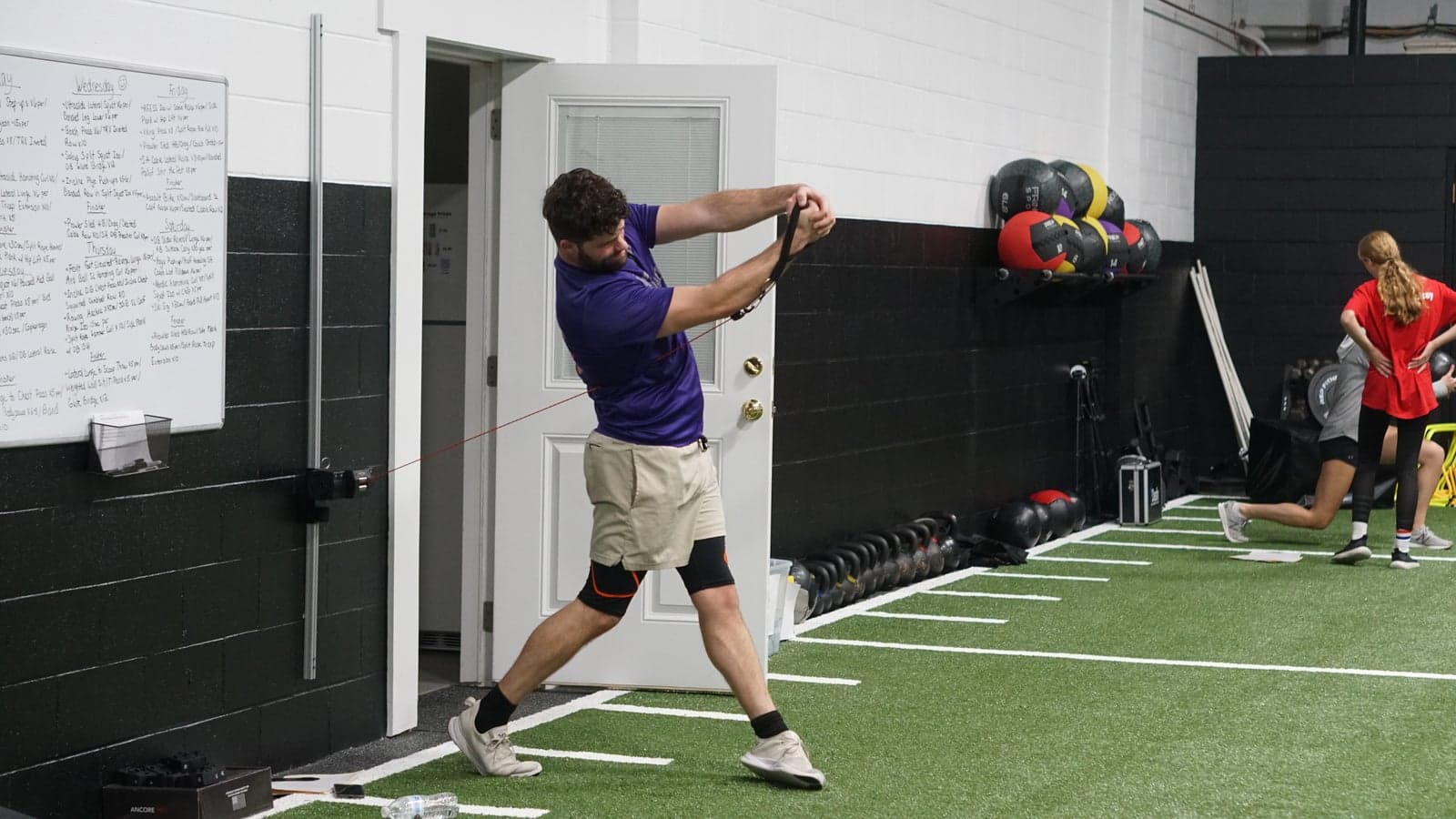A golfer rehearses his swing against a resistance cable on the turf